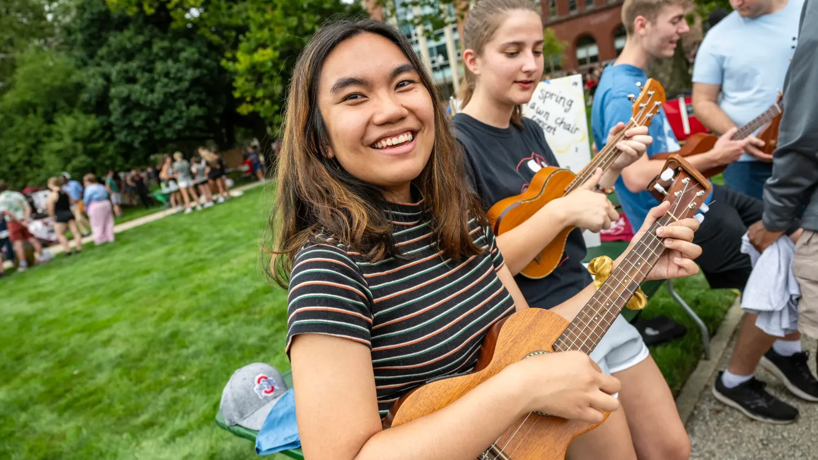 Smiling students playing ukuleles outside on the lawn
